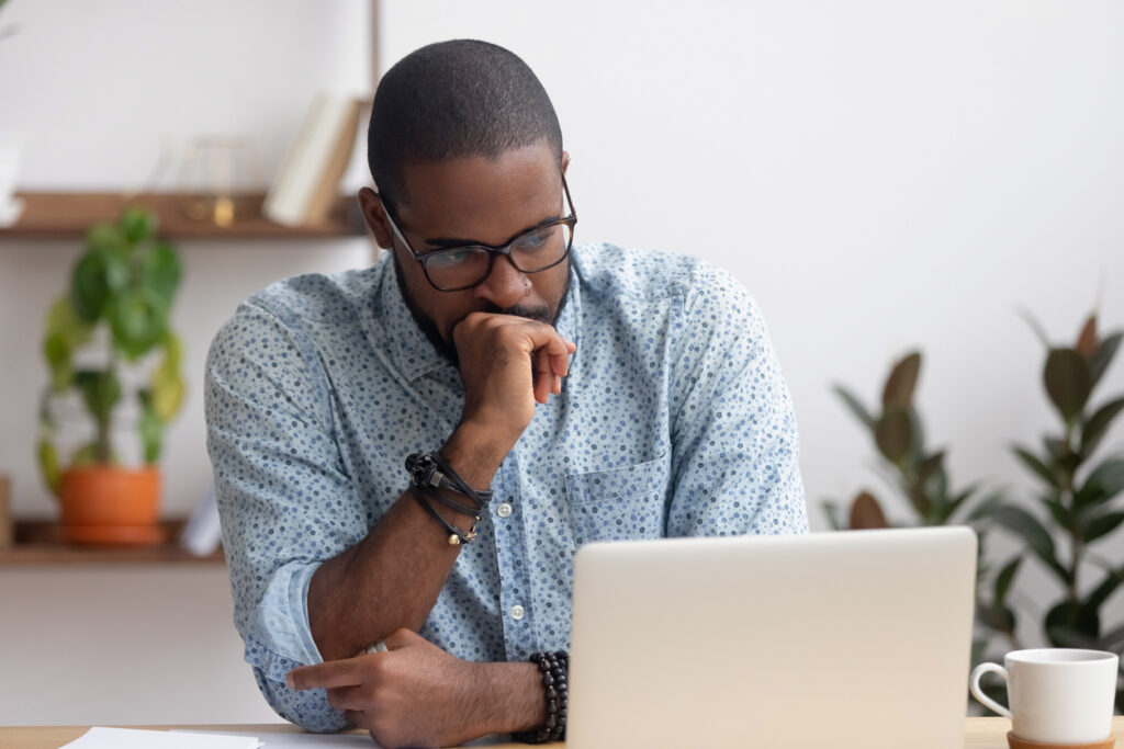 A young office manager sits deep in thought in front of his laptop.