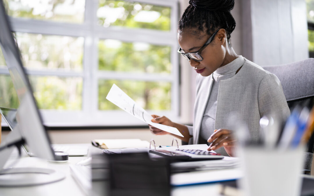 A young accountant looks at spreadsheets and inputs numbers into a calculator.