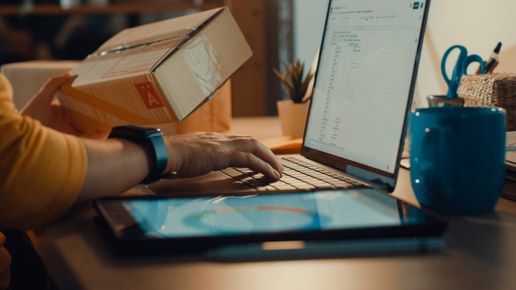 A young e-commerce business owner looks at a package and his laptop.