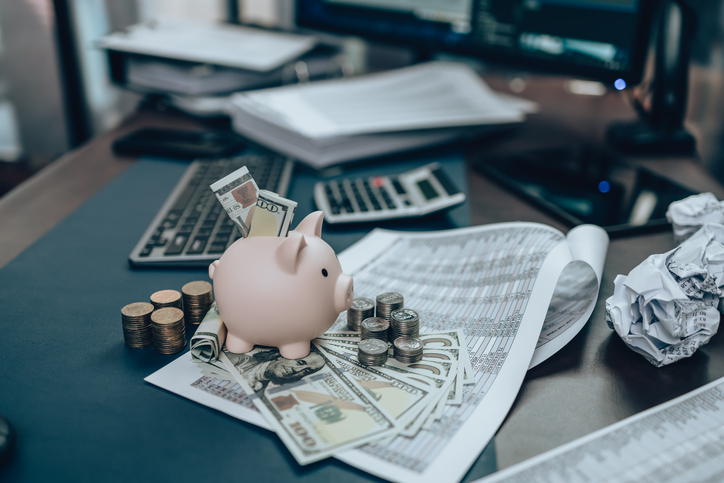 Piggy bank with cash, coins, and financial documents on a cluttered desk, symbolizing savings, budgeting, and financial planning.