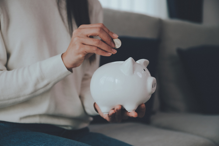 A person placing a coin into a white piggy bank.