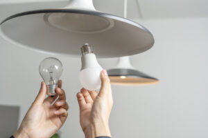 Two people replace fluorescent light bulbs (CFL) with new LED bulbs