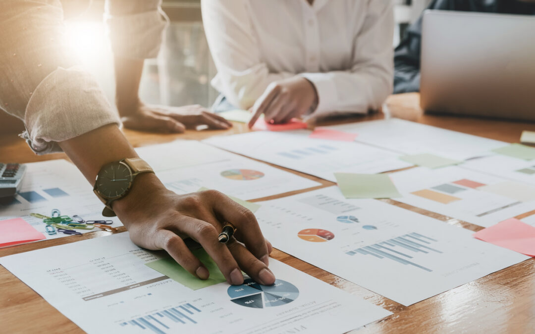 A group of business people around a table go over documents and charts.