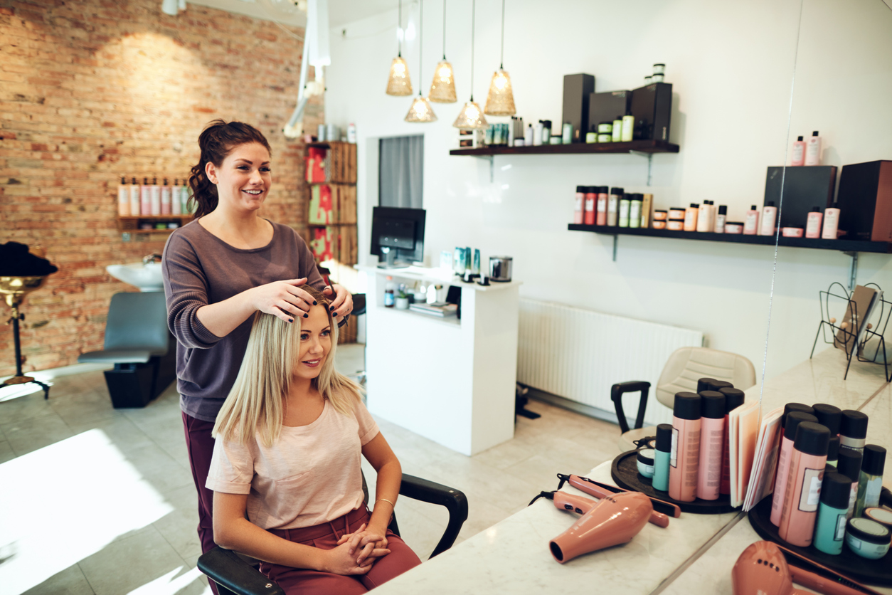 A young hairdresser starts working on a blonde woman's hair in the salon.